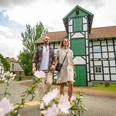 Ein Paar spaziert vor einer Fachwerk-Gutswassermühle, mit blühenden Blumen im Vordergrund.