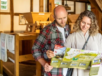 Gutswassermühle Hudenbeck Ein Paar studiert eine Landkarte in einer historischen Mühle mit Holzbalken und traditionellen Maschinen.
