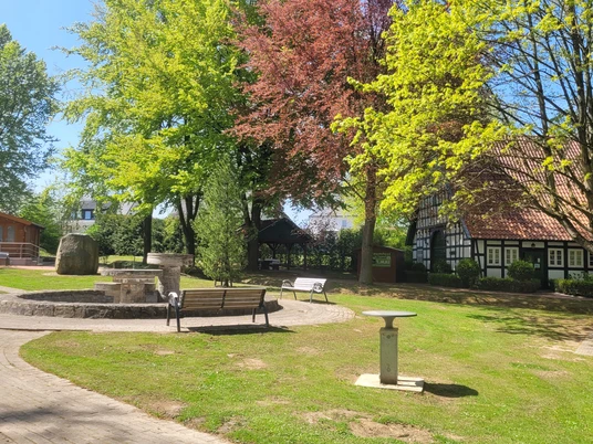 Minigolfplatz Börninghausen Offener Minigolfplatz mit Bäumen und Fachwerkhaus im Hintergrund, Wege und Sitzbänke vorhanden.