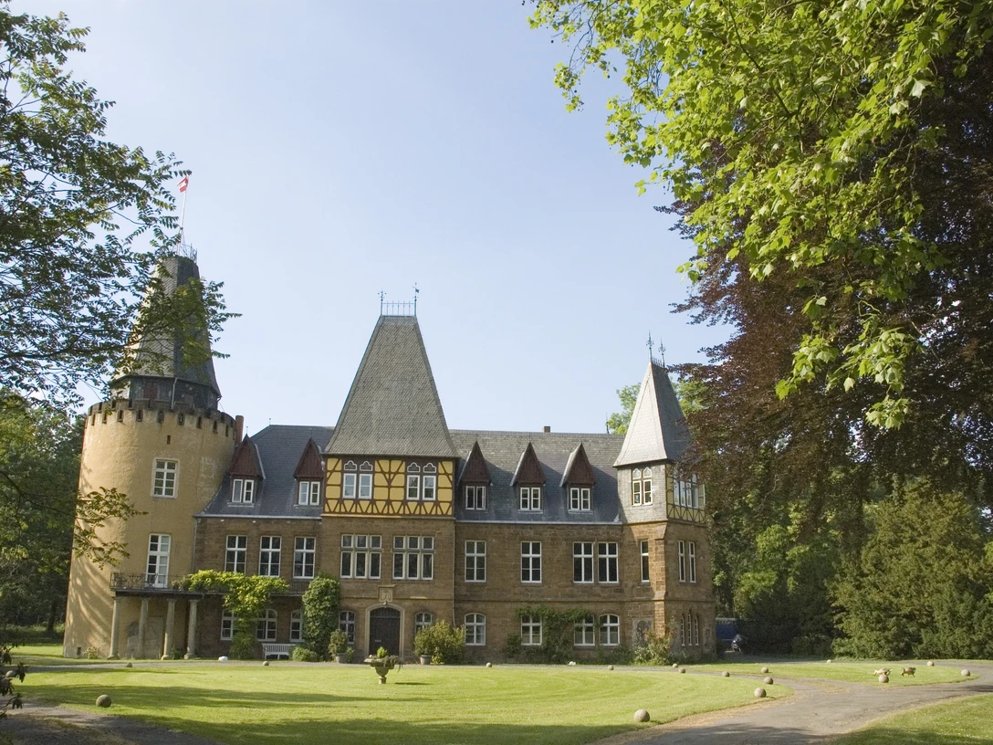 Historisches Schloss mit beeindruckenden Türmen, umgeben von gepflegten Rasenflächen und Bäumen.
