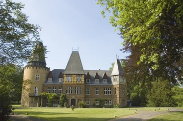 Schloss Hollwinkel Historisches Schloss mit beeindruckenden Türmen, umgeben von gepflegten Rasenflächen und Bäumen.