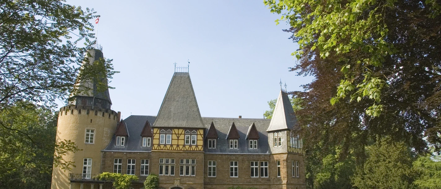 Schloss Hollwinkel Historisches Schloss mit beeindruckenden Türmen, umgeben von gepflegten Rasenflächen und Bäumen.