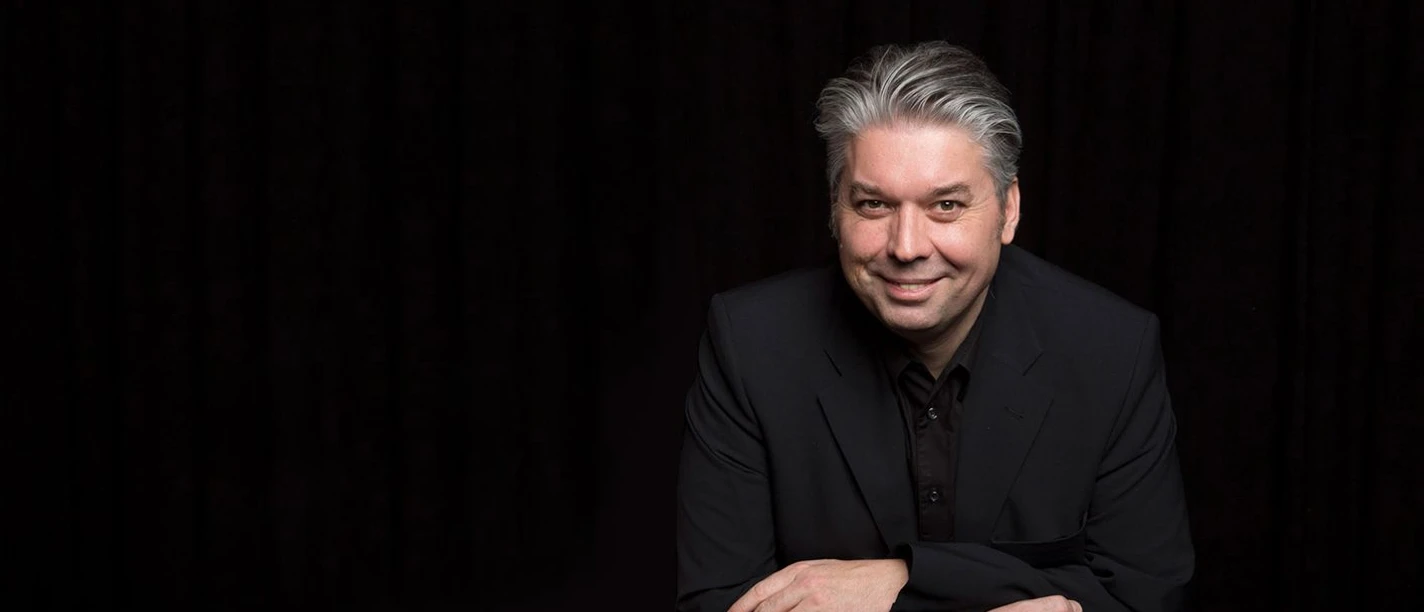 Mann mit Anzug stützt sich auf seine Ellbogen und lächelt in die Kamera.