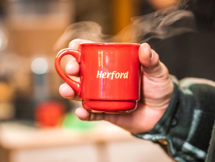 ProHerford_Weihnachtsmarkt2023_lowres_133.jpg Rote Tasse mit "Herford" Aufschrift in einer Hand, aus der Tasse steigt heißer Dampf auf.
