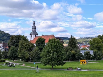 Die katholische Kirche in Beverungen erhebt sich vor einem bewaldeten Hügel unter blauem Himmel.