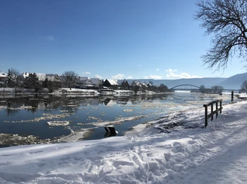 Das Foto zeigt die Weser im Winter bei Beverungen. Der Fluss ist teilweise mit Eisschollen bedeckt, im Schnee eingehüllt, und im Hintergrund ist die Weserbrücke zu sehen.