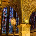 Innenaufnahme des Aachener Doms mit seinen bunten, hohen Fenstern und goldverzierter Decke und Säulen.