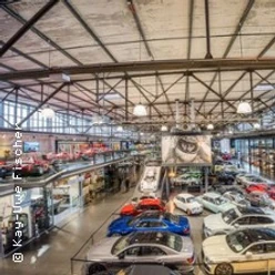 Eine beeindruckende Halle mit zahlreichen Oldtimern und Luxusfahrzeugen, umgeben von industriellem Charme.