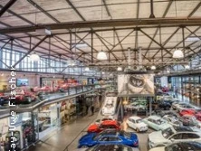 Eine beeindruckende Halle mit zahlreichen Oldtimern und Luxusfahrzeugen, umgeben von industriellem Charme.