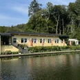 Café-Restaurant Uelfetal - Außenansicht Gelbes Gebäude am Seeufer mit Terrasse und orangenen Sonnenschirmen, umgeben von grünem Wald.