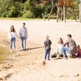 Badesee Hille Familien und Paare genießen einen sonnigen Tag am Sandstrand eines ruhigen Sees mit Spielplatz.