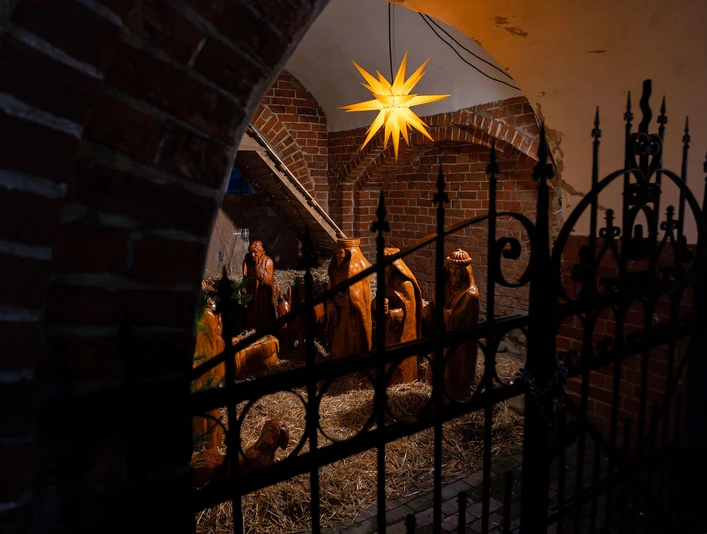 markt-im-advent-weihnachtsmarkt-krippe-st-johannes-kirche.jpg Holzkrippe mit biblischen Figuren unter gelbem Stern vor Backsteinwand in der St.-Johannes-Kirche.