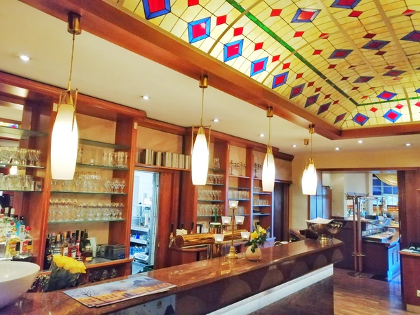 Hotelbar mit beleuchtetem Glasdach, ausgestattet mit Gläsern und Flaschen sowie einem stilvollen Tresen.