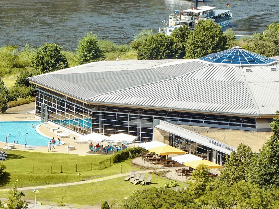 Il Ristorante Toskana Modernes Gebäude mit großem Glasdach, umgeben von Bäumen, mit einem Außenpool und einer Terrasse mit Sonnenschirmen; im Hintergrund ein Fluss.Modern building with a large glass roof, surrounded by trees, with an outdoor pool and a terrace with parasols; a river in the background.Moderní budova s velkou prosklenou střechou, obklopená stromy, s venkovním bazénem a terasou se slunečníky; v pozadí řeka.Nowoczesny budynek z dużym szklanym dachem, otoczony drzewami, z odkrytym basenem i tarasem z parasolami; w tle rzeka.Modern gebouw met een groot glazen dak, omgeven door bomen, met een buitenzwembad en een terras met parasols; een rivier op de achtergrond.Edificio moderno con ampio tetto in vetro, circondato da alberi, con piscina all'aperto e terrazza con ombrelloni; sullo sfondo il fiume.