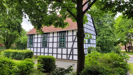 Alte Klus Espelkamp Frotheim Fachwerkgebäude inmitten von Bäumen, mit weißen Wänden und schwarzen Balken; rote Ziegeldach.