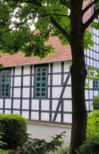 Alte Klus Espelkamp Frotheim Fachwerkgebäude inmitten von Bäumen, mit weißen Wänden und schwarzen Balken; rote Ziegeldach.