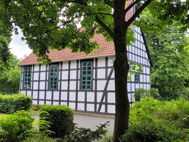 Alte Klus Espelkamp Frotheim Fachwerkgebäude inmitten von Bäumen, mit weißen Wänden und schwarzen Balken; rote Ziegeldach.