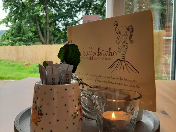 Kaffeeküche Hille Tasse und Kerze auf einem Tablett in einem Café mit Blick auf einen grünen Baum außerhalb des Fensters.