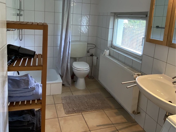 IMG_2918.jpeg Helles Badezimmer mit Dusche, Toilette, Waschbecken und Regalen, neutral gefliest und gut beleuchtet.