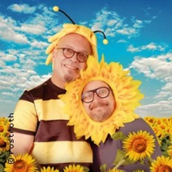 Zwei verkleidete Personen als Biene und Sonnenblume in einem Feld unter blauem Himmel.