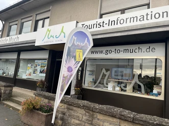 Tourist-Information Eingang der Tourist-Information Much mit Werbebanner und Schaufenstern voller Broschüren.