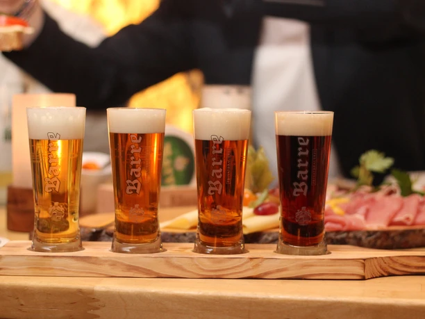 Barres Brauwelt ProBier-Brett mit vier gefüllten Biergläsern, begleitet von rustikalem Imbiss auf Holz.