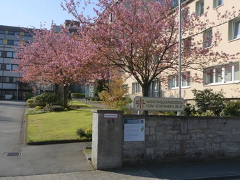 Eingang des Missionshauses Neuenbeken mit blühenden Bäumen und angrenzender Rasenfläche im Frühling.