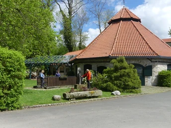 Uhdenhütte Runde Steinhütte mit rotem Ziegeldach in grüner Umgebung, Menschen unter Pavillon im Austausch.