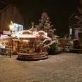 20171210_180126.jpg Ein verschneiter Weihnachtsmarkt am Abend mit beleuchtetem Karussell und geschmücktem Weihnachtsbaum.
