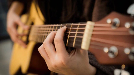 Städtische Musikschule.png Person spielt eine Akustikgitarre mit konzentriertem Gesichtsausdruck; Fokus auf Hand und Saiten.