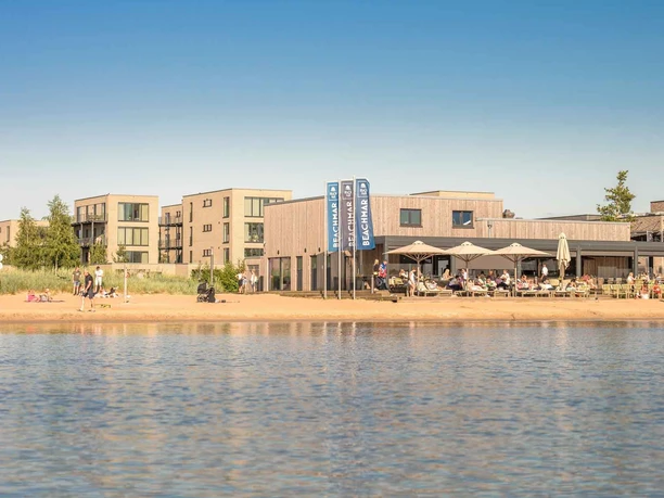 Der hauseigene Sandstrand mit dem Beach-Club Beachmar und modernen Ferienwohnungen im Hintergrund.