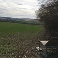 Holzbank am Rand eines grünen Feldes mit weitem Blick auf die sanft geschwungene Landschaft.
