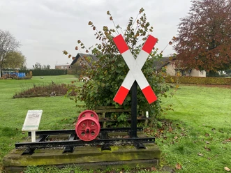 Eisenbahnkategoriekreuz mit rotem Zahnrad auf Schienen. Hintergrund: herbstliche Landschaft und Häuser.