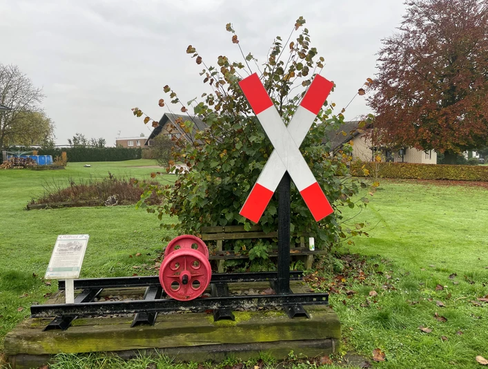 Eisenbahnkategoriekreuz mit rotem Zahnrad auf Schienen. Hintergrund: herbstliche Landschaft und Häuser.