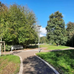 Kurpark Levern Parkweg mit Bäumen und Bänken unter blauem Himmel, von Laternen entlang des Weges gesäumt.