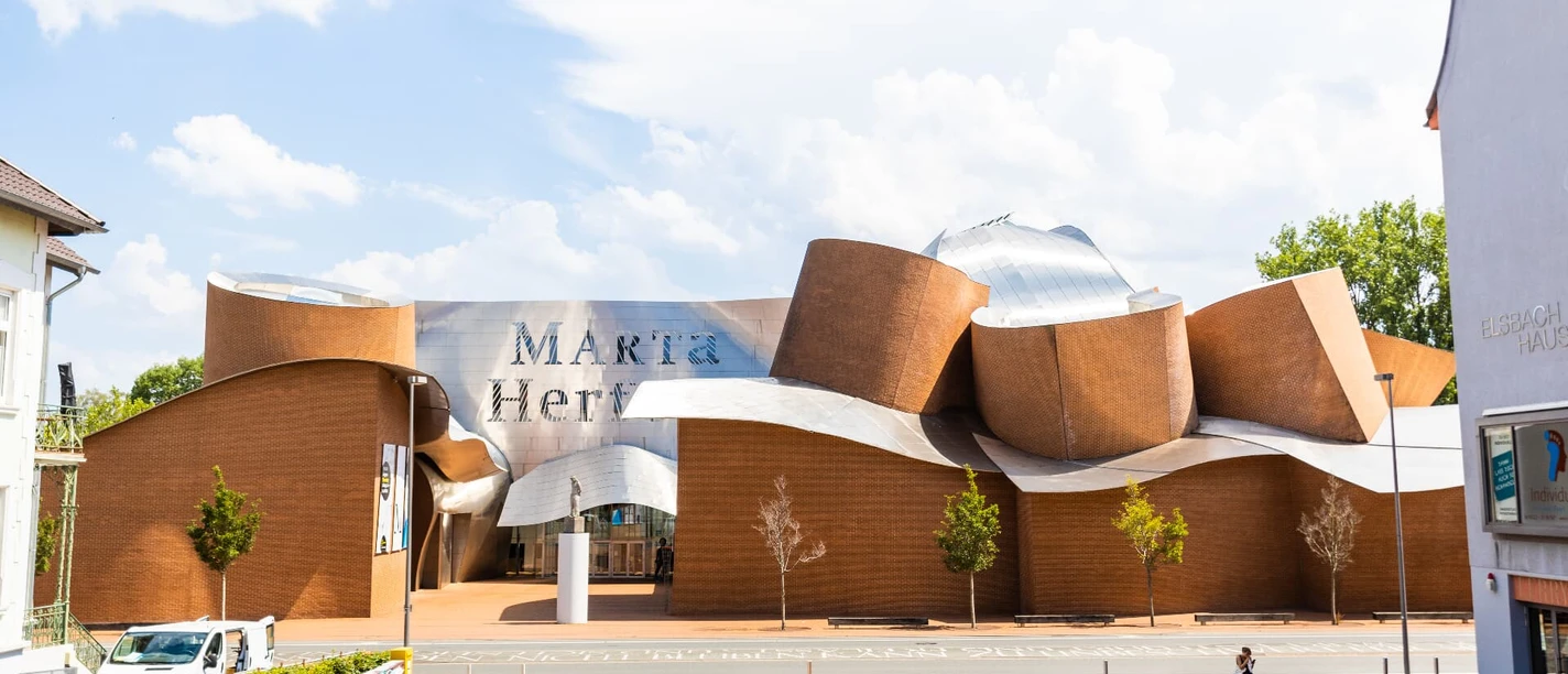 Museum Marta Herford mit seiner wellenförmigen Fassade aus Backstein und Stahl, bei sonnigem Wetter.