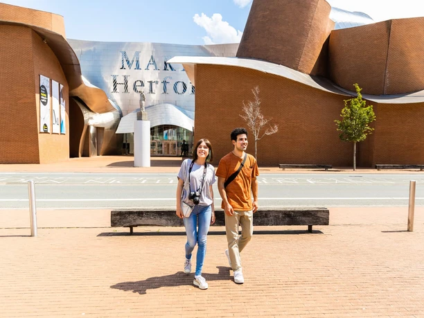 herford-marta-herford-teutoburger-wald-tourismus-h-tornow-012-jpg.jpg Außenansicht des Museums Marta Herford mit zwei lächelnden Menschen auf einem breiten Gehweg.