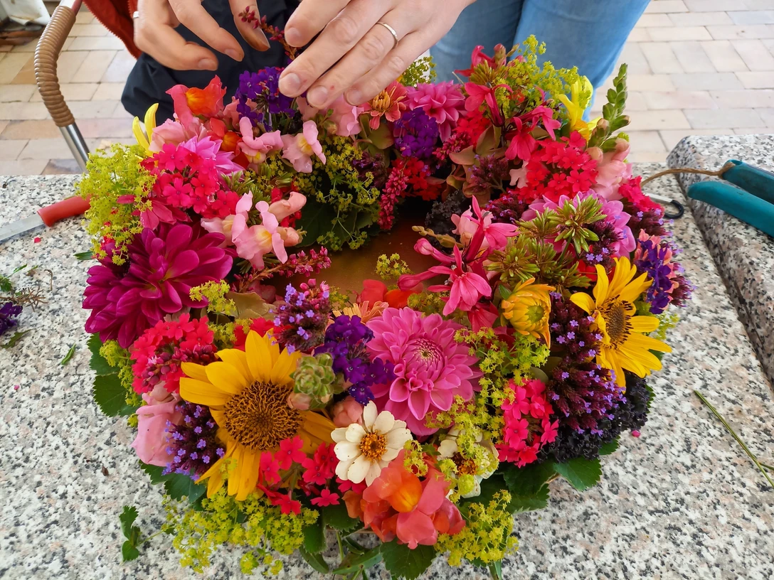 06.10.2025 Ursel Kruse.jpg Bunte Sommerblumen werden zu einem farbenprächtigen Kranz auf einem Steintisch arrangiert.