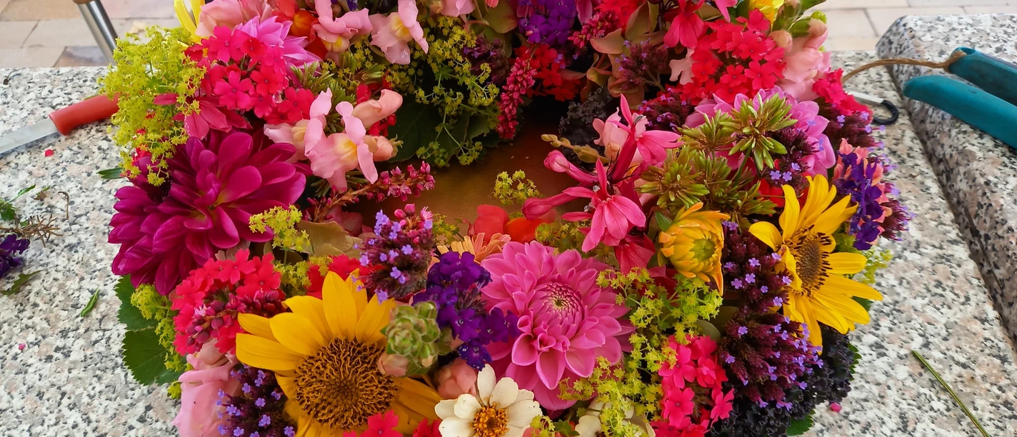 06.10.2025 Ursel Kruse.jpg Bunte Sommerblumen werden zu einem farbenprächtigen Kranz auf einem Steintisch arrangiert.