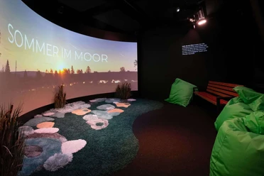 Kinoraum in der Moorerlebniswelt mit Leinwand und Sitzecke.