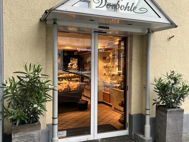 Eingangsbereich eines Cafés mit gläserner Tür, dekoriert mit Pflanzen in modernen Kübeln.