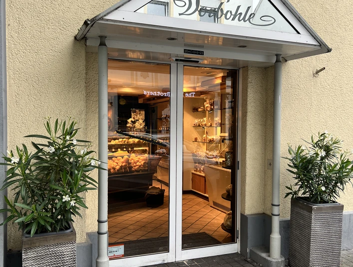 Eingangsbereich eines Cafés mit gläserner Tür, dekoriert mit Pflanzen in modernen Kübeln.