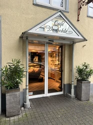Vorbohle 2 Eingangsbereich eines Cafés mit gläserner Tür, dekoriert mit Pflanzen in modernen Kübeln.