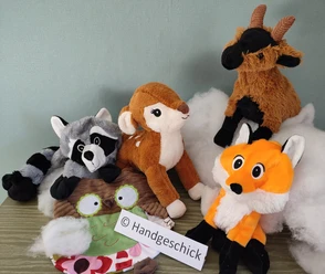 Various cuddly toys, including a raccoon and a fox, are placed on a table in front of a green wall.