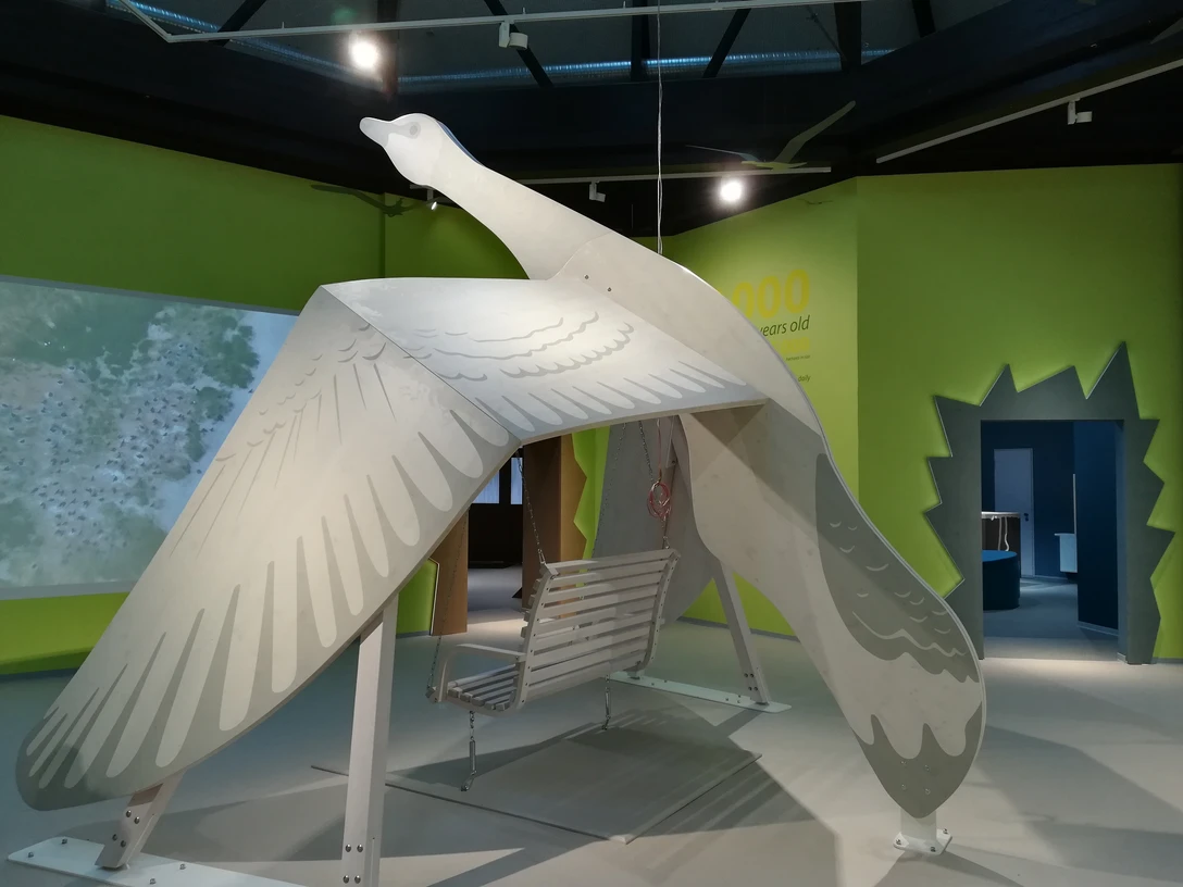 Nationalpark-Haus Greetsiel Große Holzskulptur einer fliegenden Gans mit Schaukel darunter in einer modernen Ausstellungshalle.