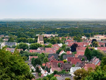 Blick auf eine idyllische Kleinstadt mit roten Dächern, üppigen Bäumen und einer Kirche in der Mitte.