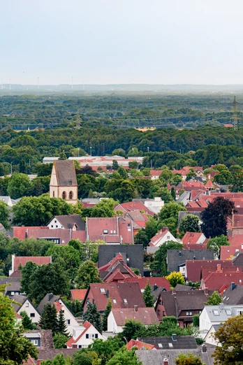 Blick auf Halle (Westf.) Blick auf eine idyllische Kleinstadt mit roten Dächern, üppigen Bäumen und einer Kirche in der Mitte.