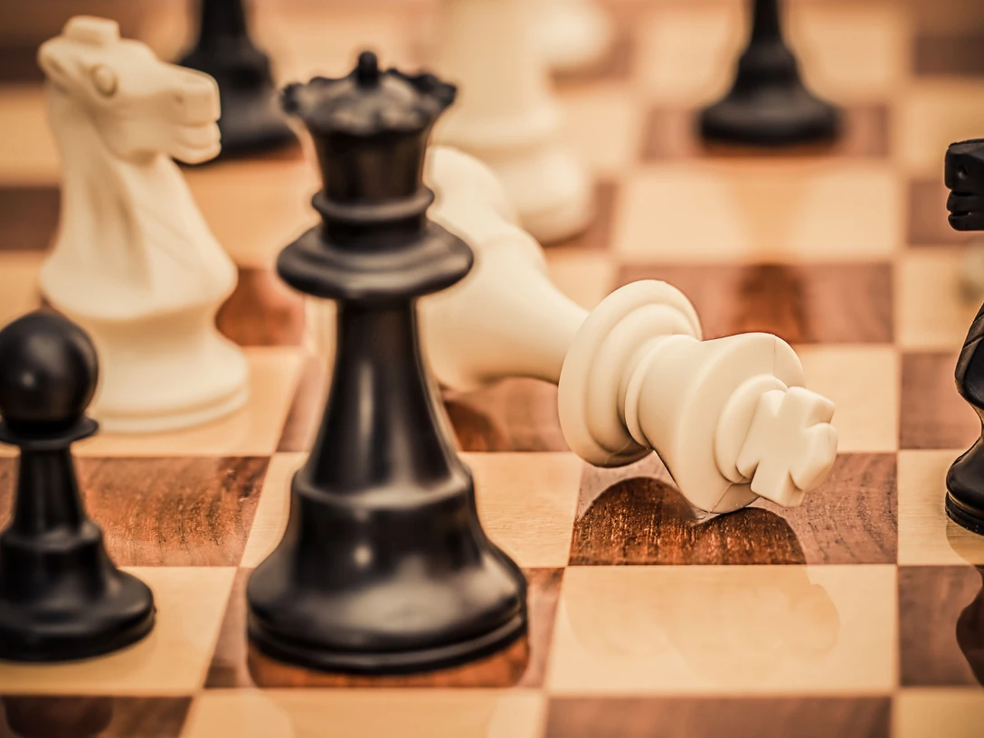 Schachtuerkencup_HNF.jpg Schachbrett mit fokussierter Perspektive auf umgefallenen weißen König, umgeben von Figuren im Spiel.