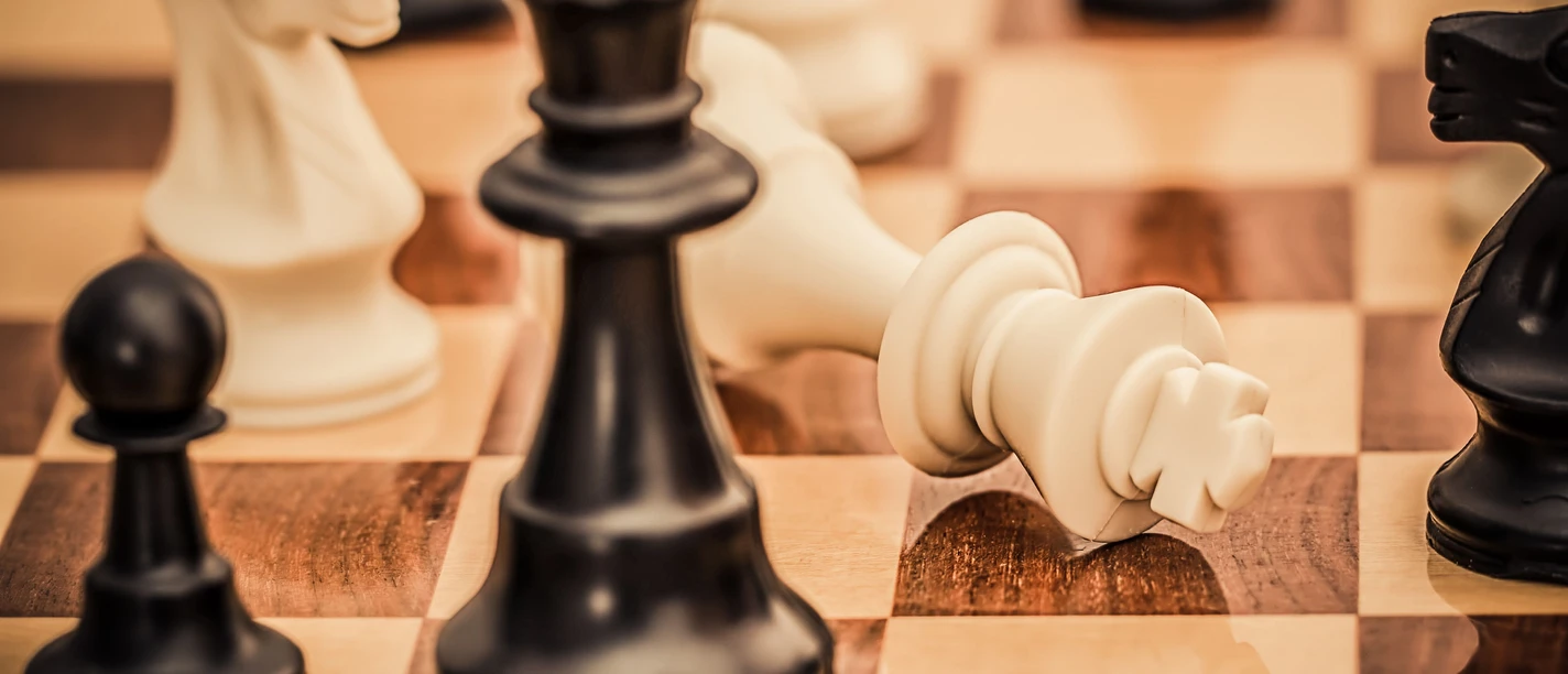 Schachtuerkencup_HNF.jpg Schachbrett mit fokussierter Perspektive auf umgefallenen weißen König, umgeben von Figuren im Spiel.