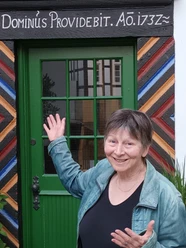 stadtrundgang_bild_selbitschka.jpg Frau in grüner Jacke präsentiert lachend eine rustikale Tür mit farbenfrohen Holzmuster.